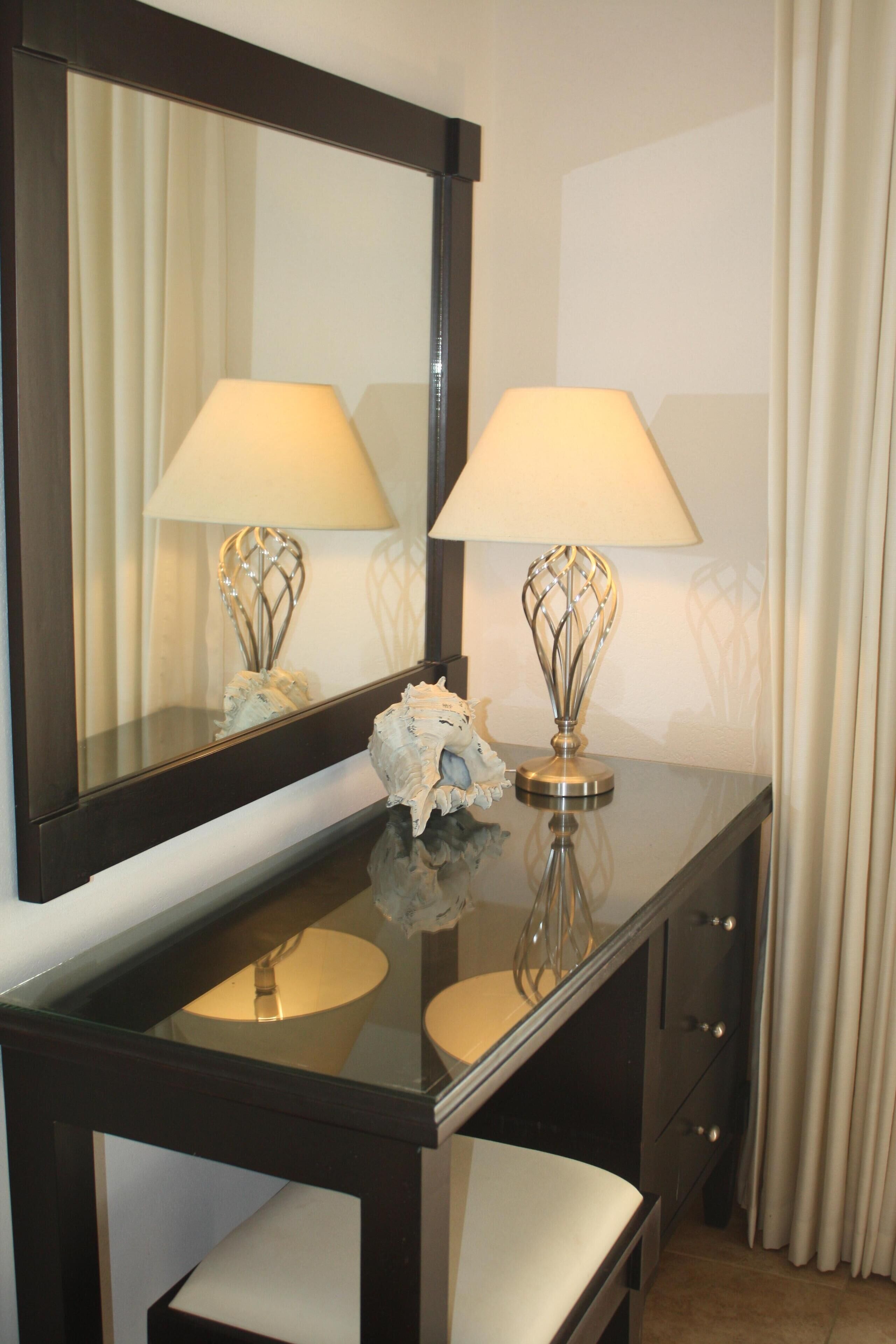 A hotel room vanity with a large mirror, two lamps, and a decorative shell.