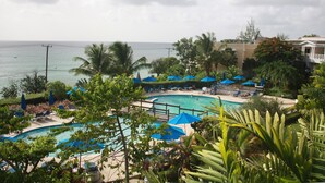 A pool area with blue umbrellas, lounge chairs, and a view of the ocean.