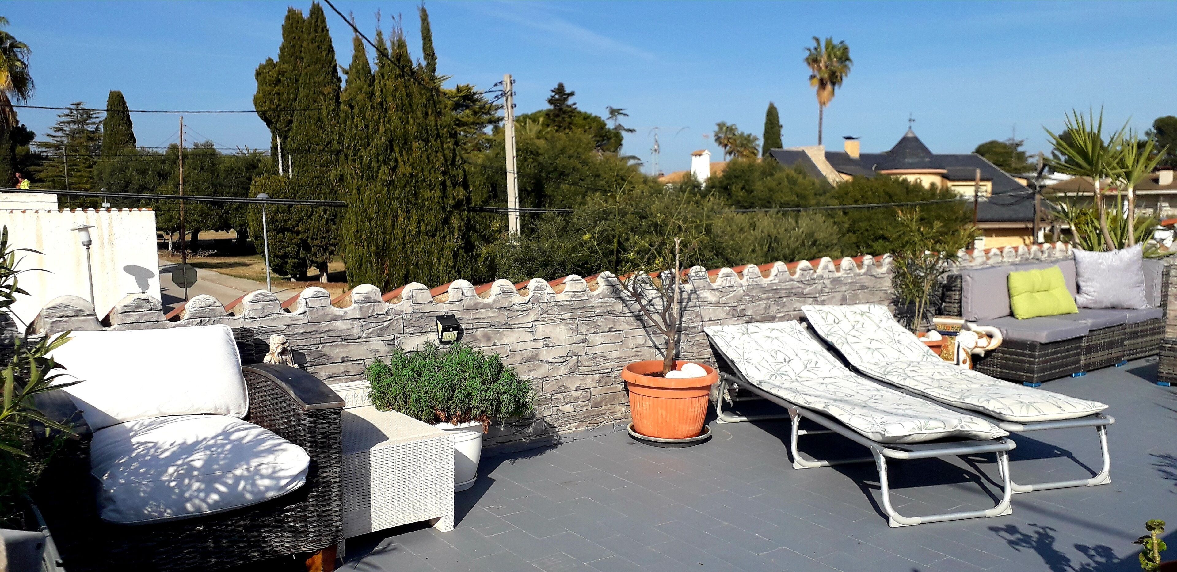 Une terrasse sur le toit, aménagée avec des meubles en osier, un mur en pierre et des plantes en pot.