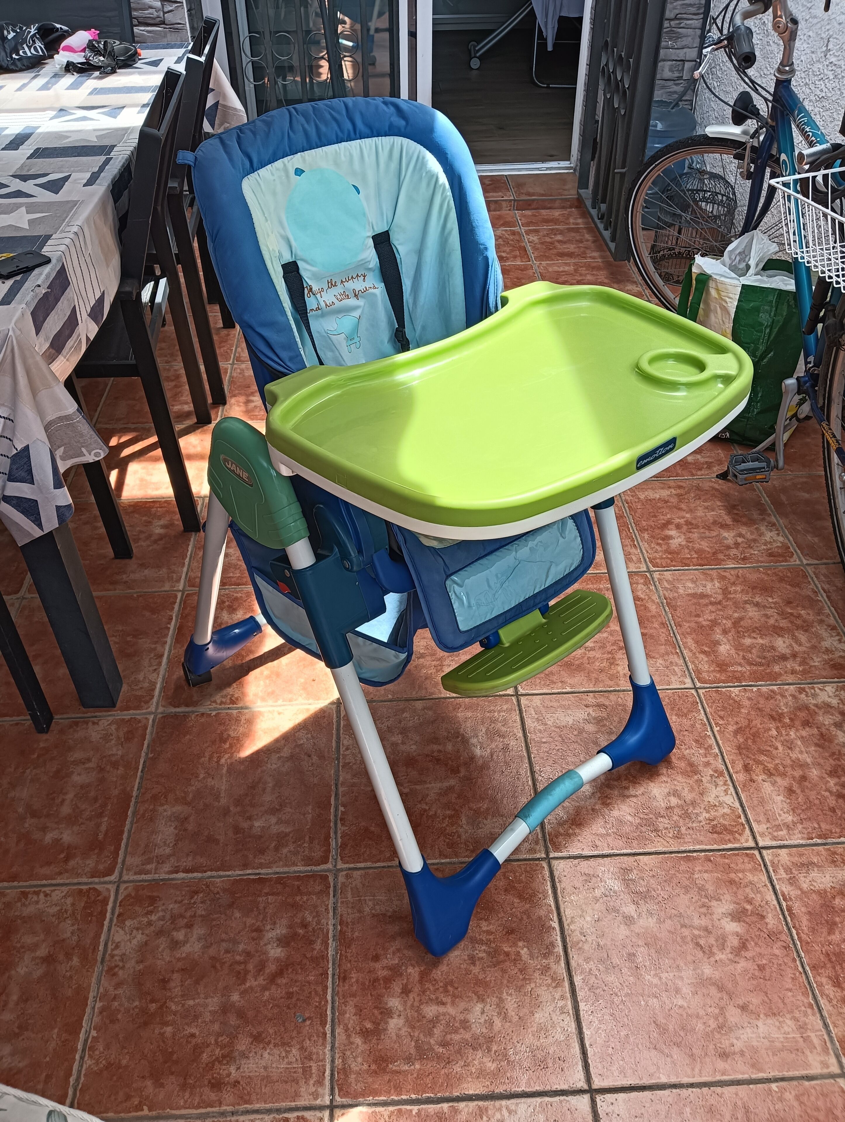 A baby high chair with a green tray, blue and white legs, and a blue cushion with a dolphin design.