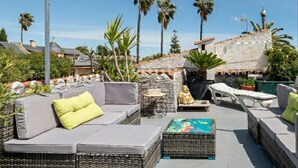 An outdoor seating area with wicker furniture, a Buddha statue, and a view of palm trees and buildings.