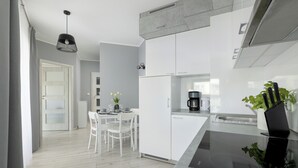 A modern kitchen with white cabinetry, a black countertop, and a dining area with white chairs and a table. - Comfortable 36 m² apartment with balcony, bedroom and modern furnishings. (Świnoujście)