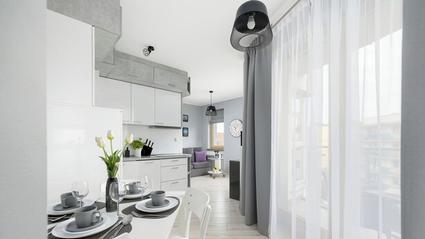 A modern kitchen with white cabinets, a dining area with a table set for four, and a large window with sheer curtains. - Comfortable 36 m² apartment with balcony, bedroom and modern furnishings. (Świnoujście)