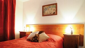Habitación de hotel con cabecera de madera, colcha roja, un osito de peluche sobre las almohadas y un cuadro en la pared.