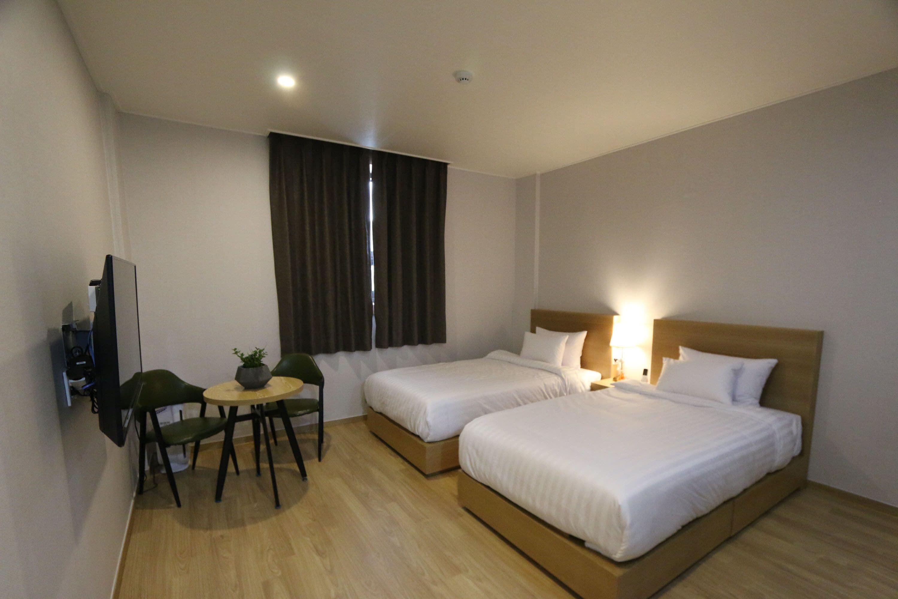 A hotel room with two beds, a desk with a chair, a small table with a plant, and a TV.