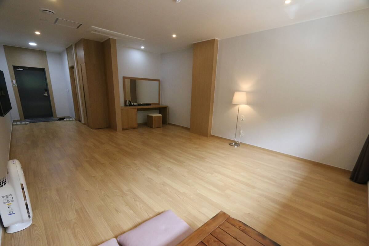 A hotel room with a wooden floor, a bed, a bedside table, a lamp, and a large mirror.