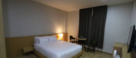 A hotel room with a wooden bed, a desk, a chair, a TV, and a window with curtains.