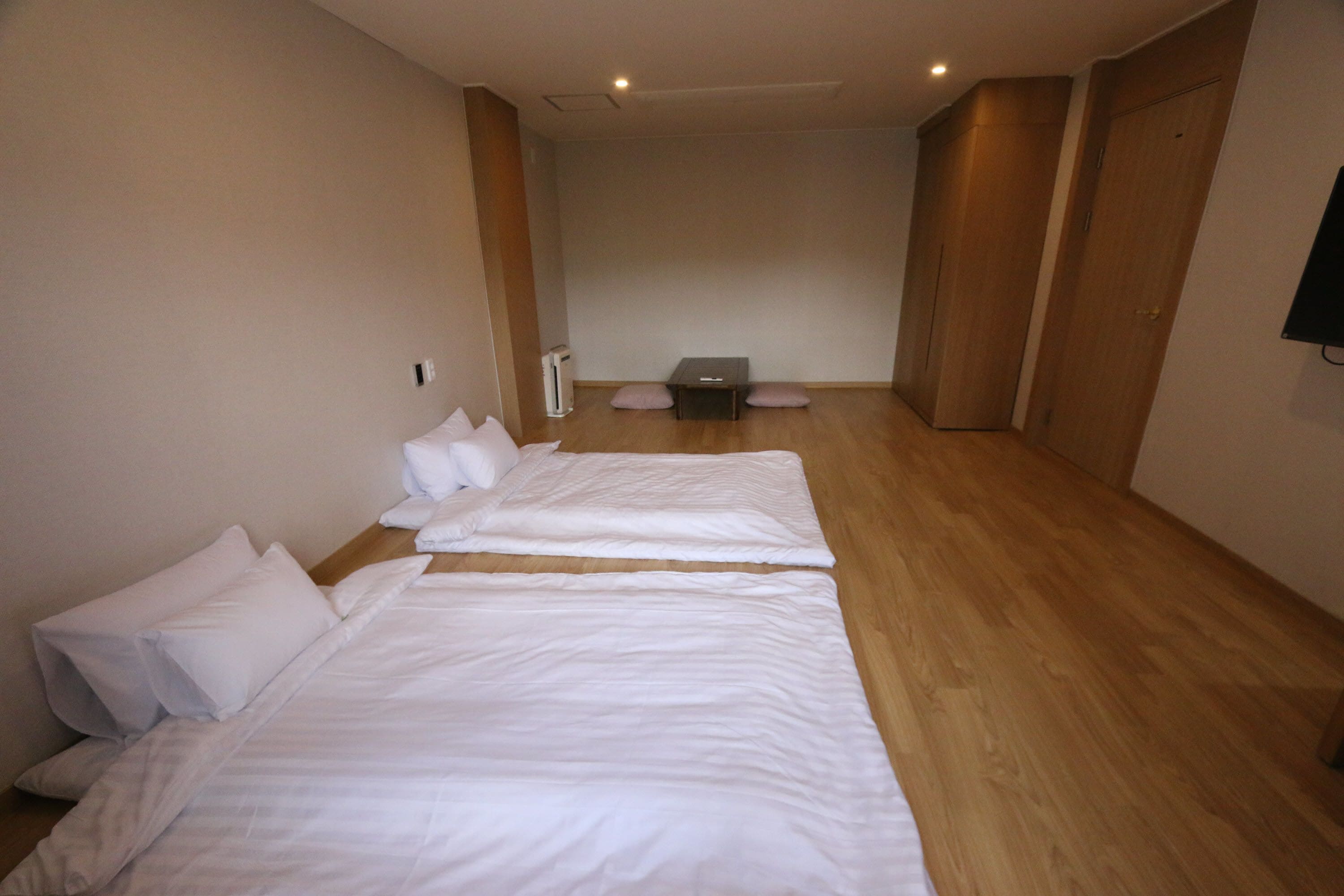 A hotel room with two beds, a small table, and a TV on the wall.