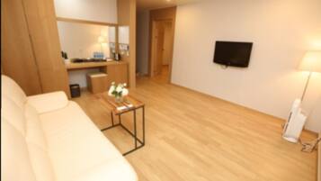 Una sala de estar moderna con un sofá blanco, una mesa de centro de madera con flores, un televisor de pantalla plana montado en la pared y una lámpara.