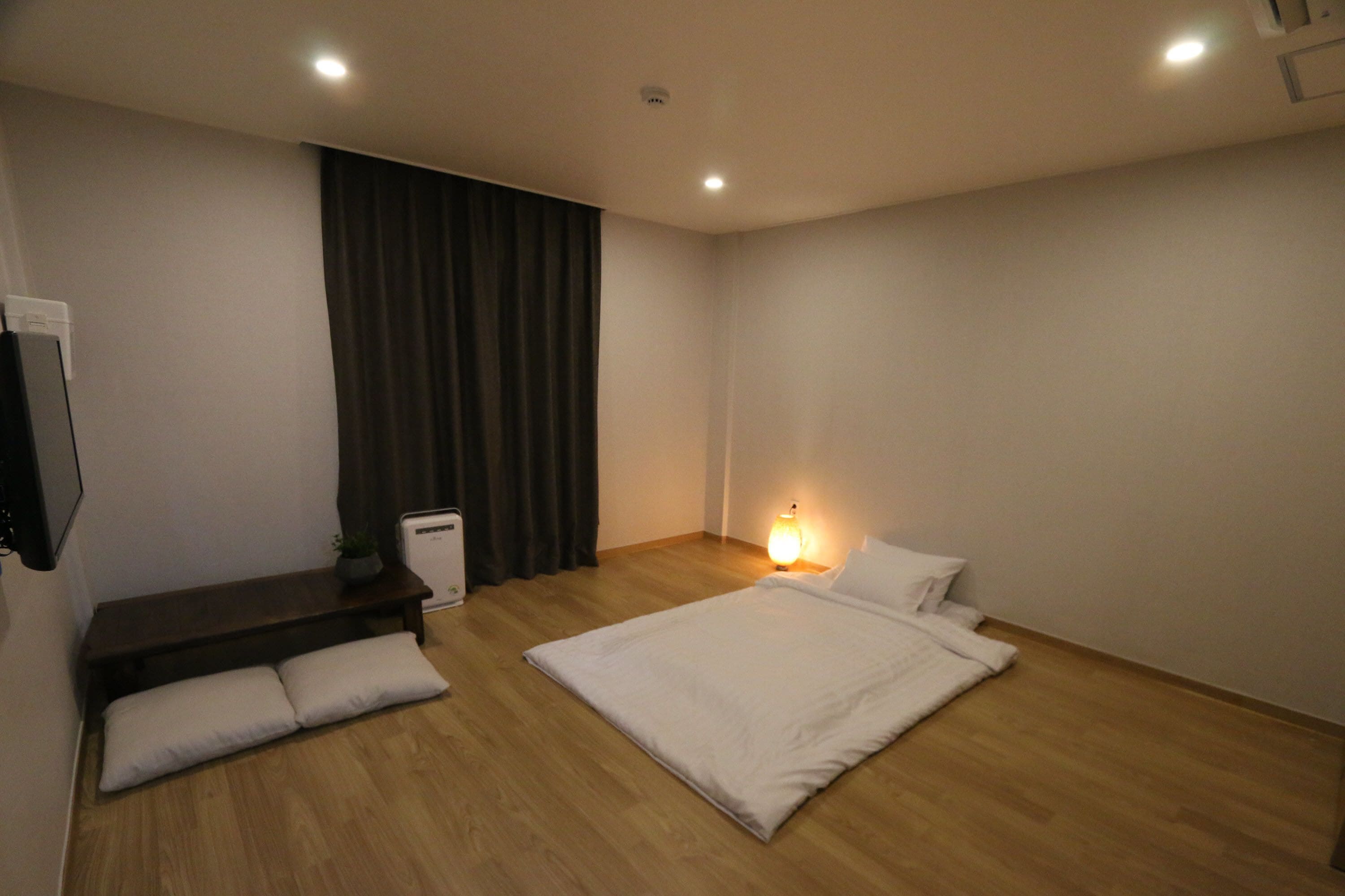 Una camera da letto con un letto, un comodino, una lampada e una panca con cuscini.