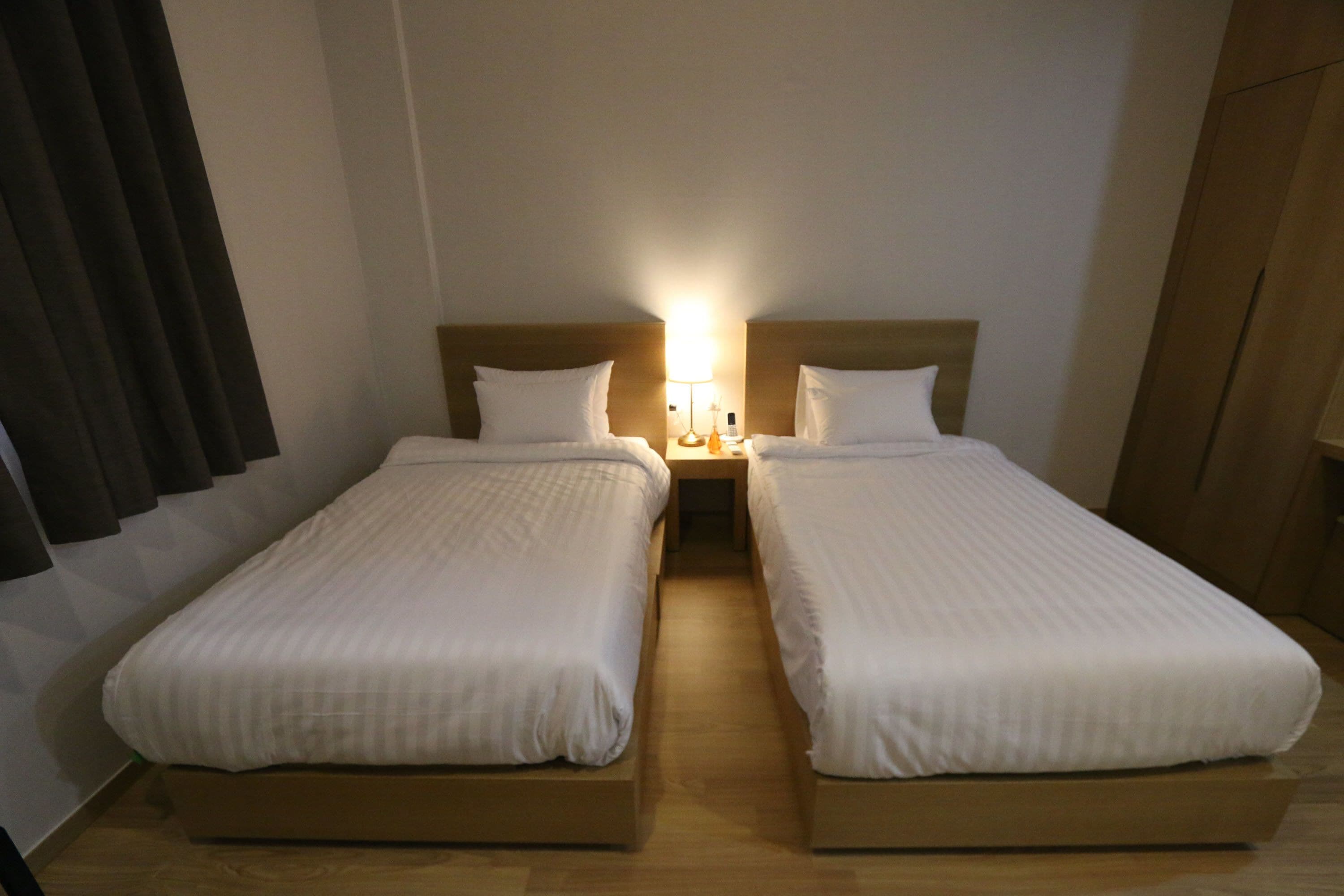 Una camera d'albergo con due letti singoli, un comodino con una lampada e un armadio in legno.