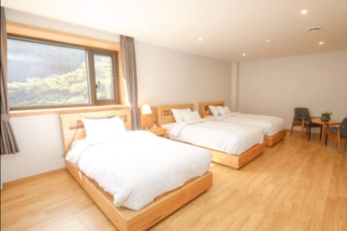 A hotel room with two beds, a small table, a chair, and a window with a view of trees.