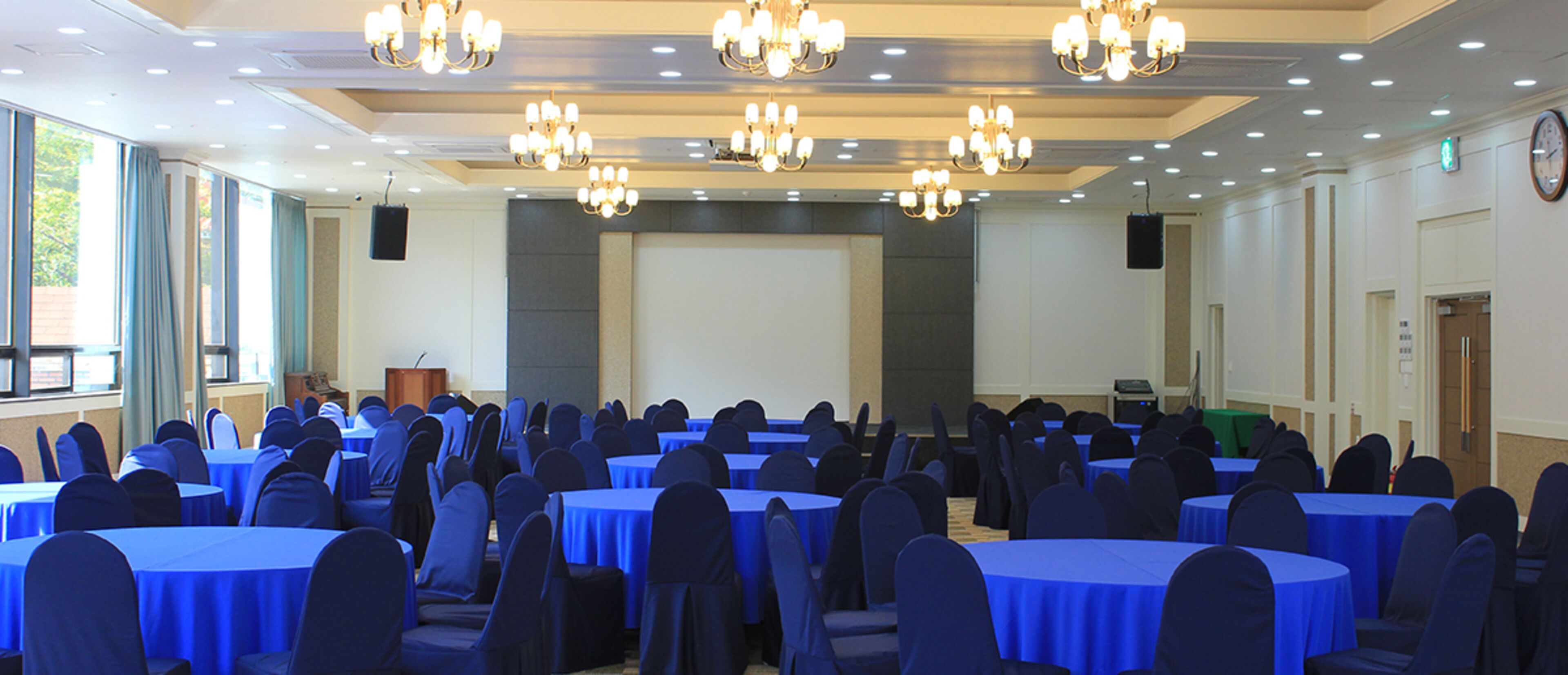 Un salón de conferencias con mesas redondas, manteles azules y sillas oscuras.