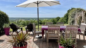 An outdoor patio with a table and chairs, surrounded by potted plants and a view of the countryside.