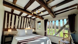 A bedroom with a large bed, wooden beams, a window with a view of trees, and a chair.