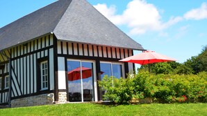 A half-timbered building with a steeply pitched roof, large glass doors, and a red umbrella in front.