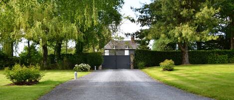 A driveway leading to a house with a dark gate, surrounded by lush greenery and trees.
