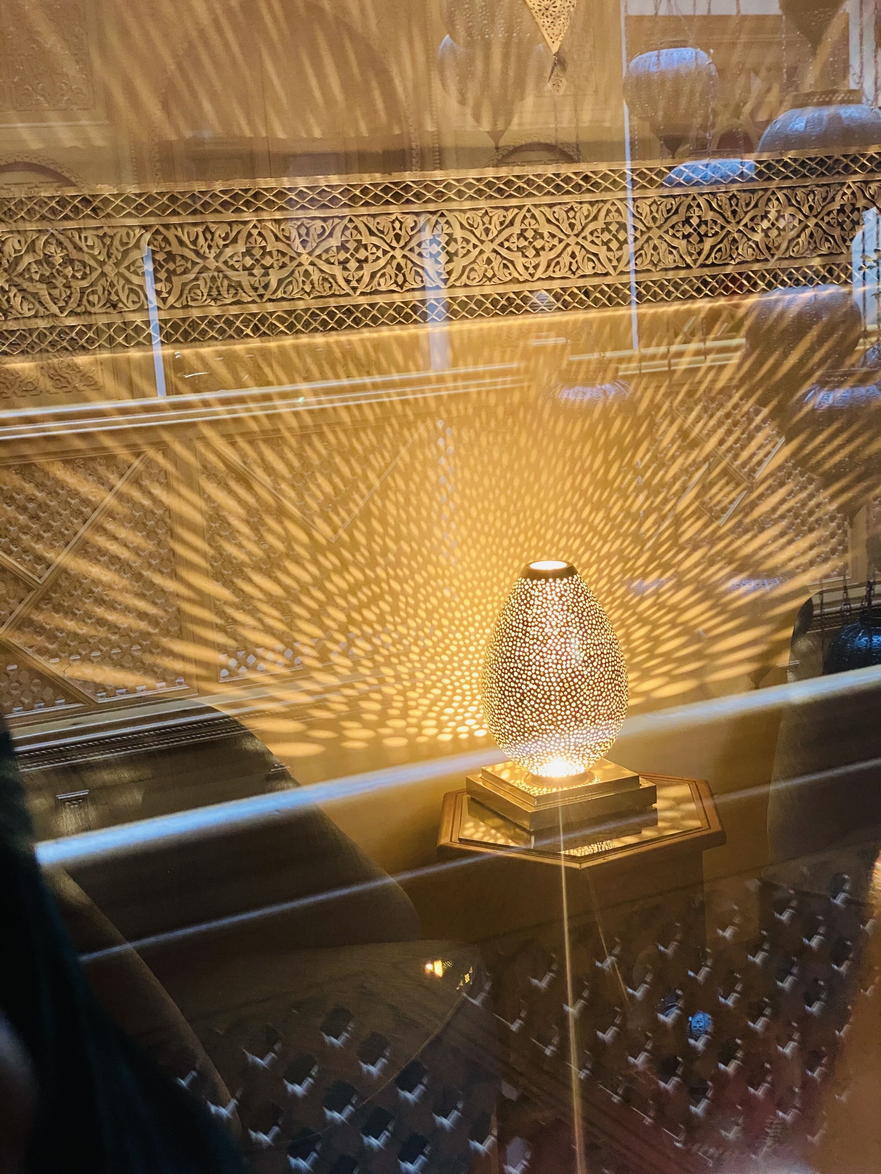 A decorative lamp with intricate patterns on a stand, set against a backdrop of ornate wall designs.