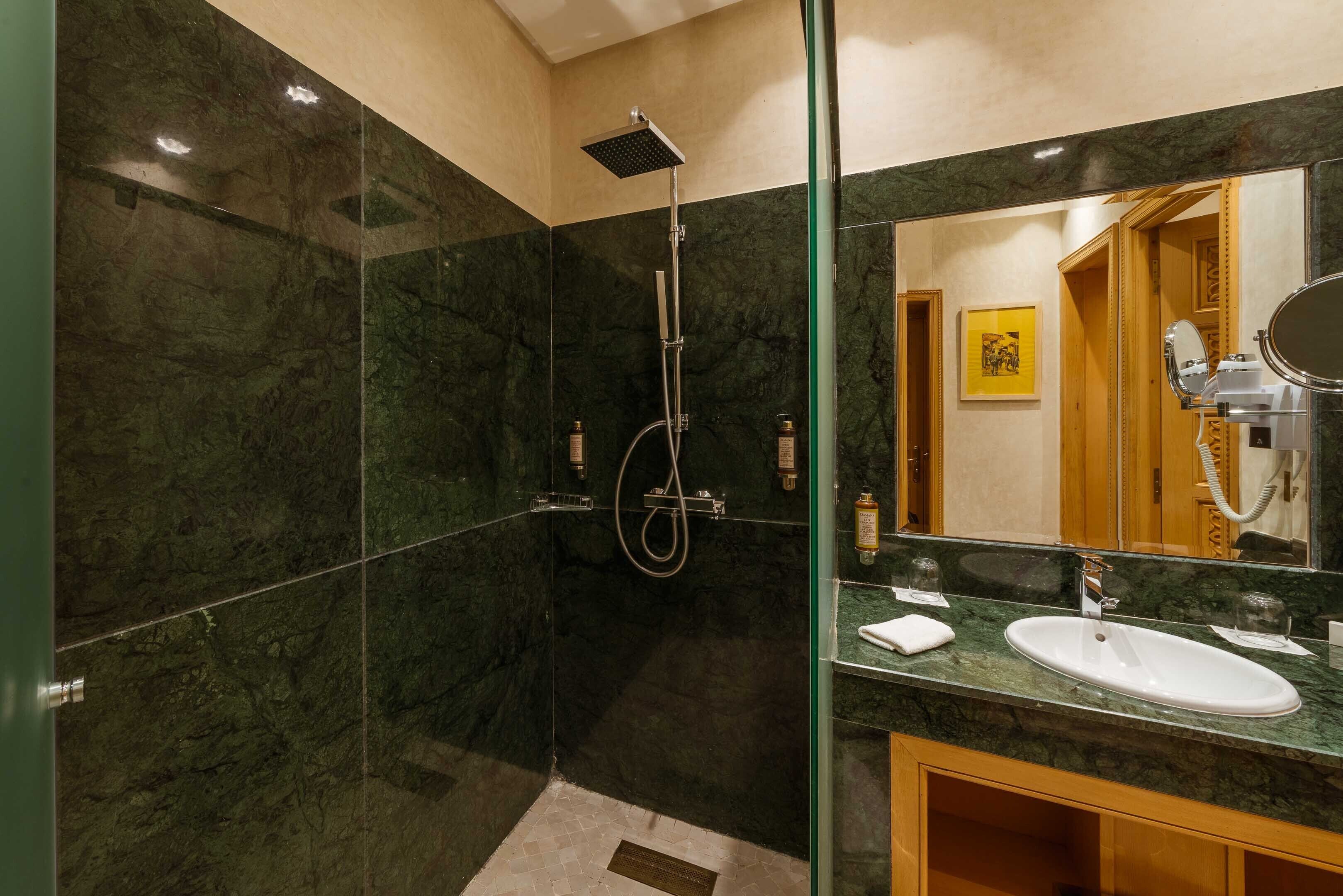Een moderne badkamer met een douchecabine van glas, een marmeren aanrechtblad en een grote spiegel.