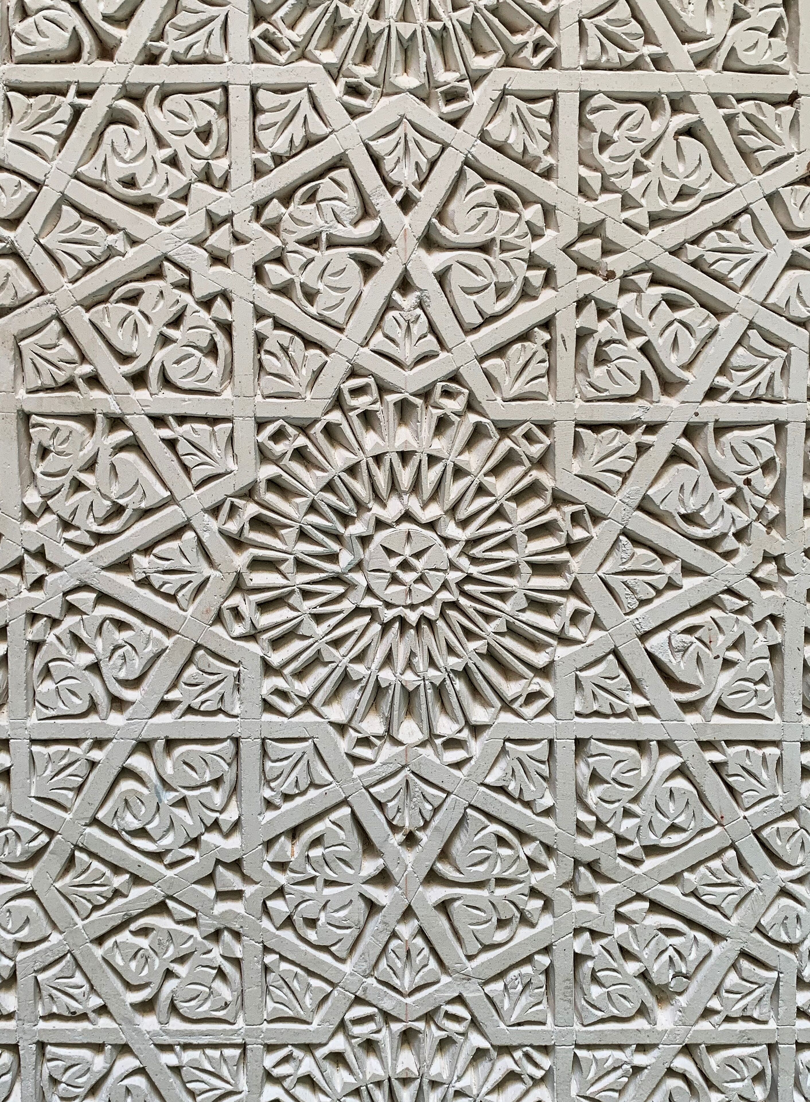 Ein detailliertes geometrisches Muster mit einem zentralen floralen Motiv, vermutlich Teil einer Gebäudefassade oder Innenarchitektur.