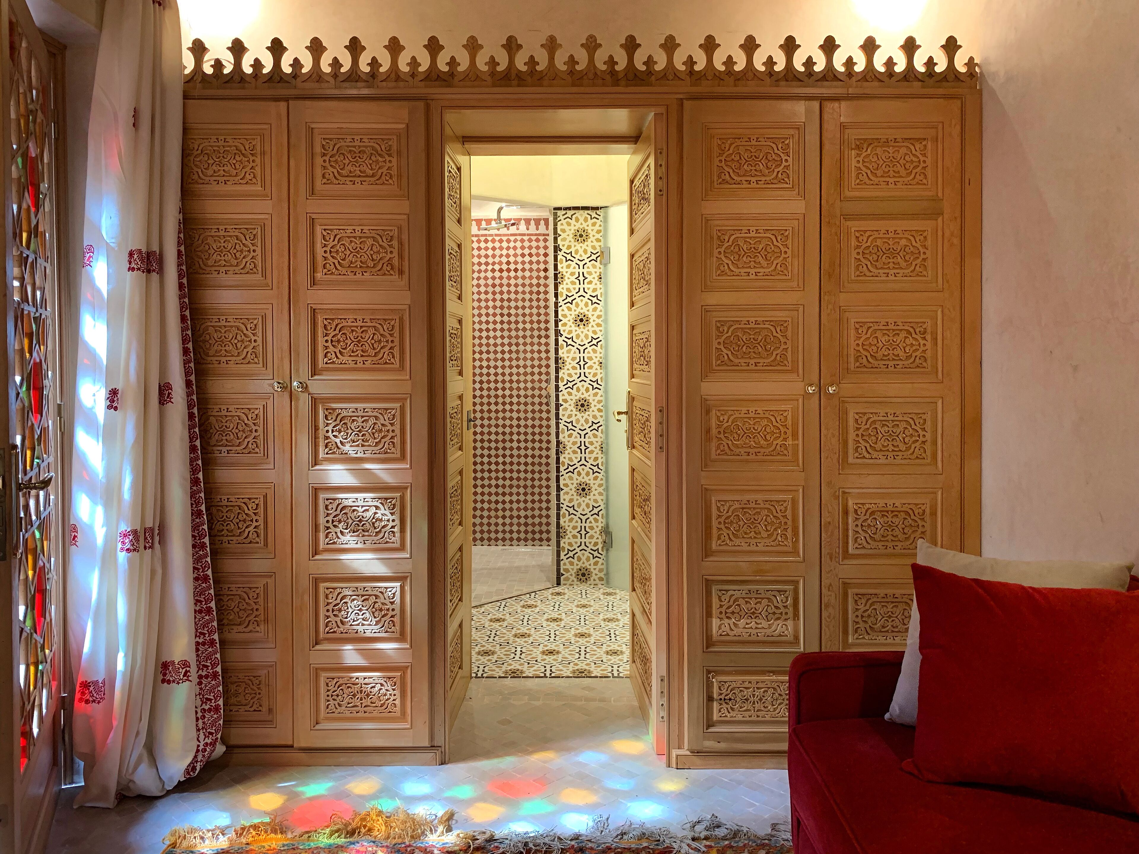 Ein Zimmer mit einer Holztür, aufwändigen Schnitzereien, einer Wand mit Muster und einem roten Sofa.
