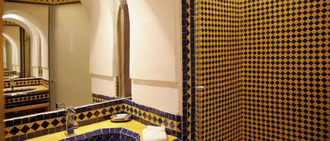 A bathroom with a yellow and blue tiled sink, a mirror, and a shower with a diamond pattern.