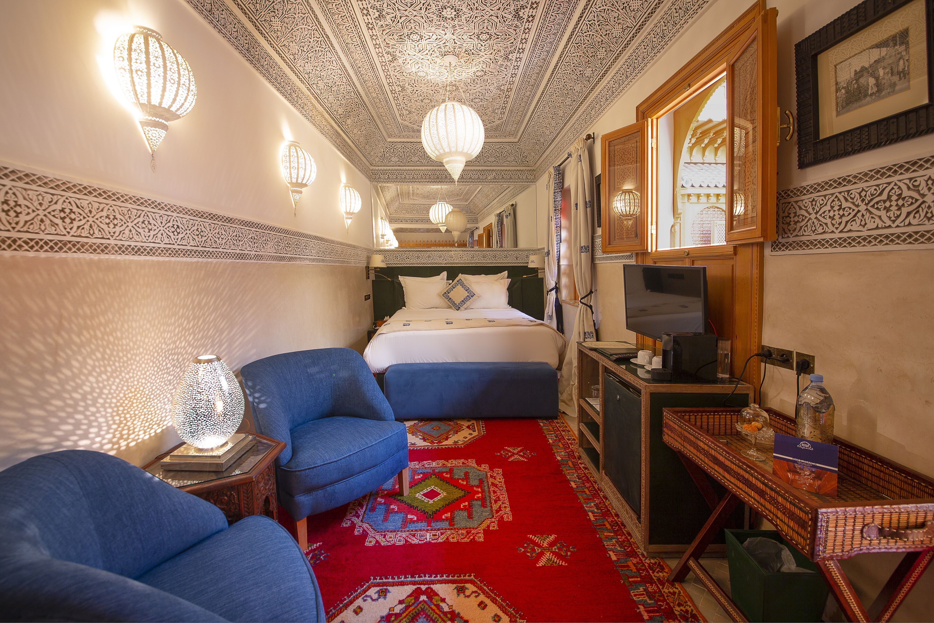 Une chambre d’hôtel avec un lit, un bureau, une chaise, une lampe et une moquette à motifs.