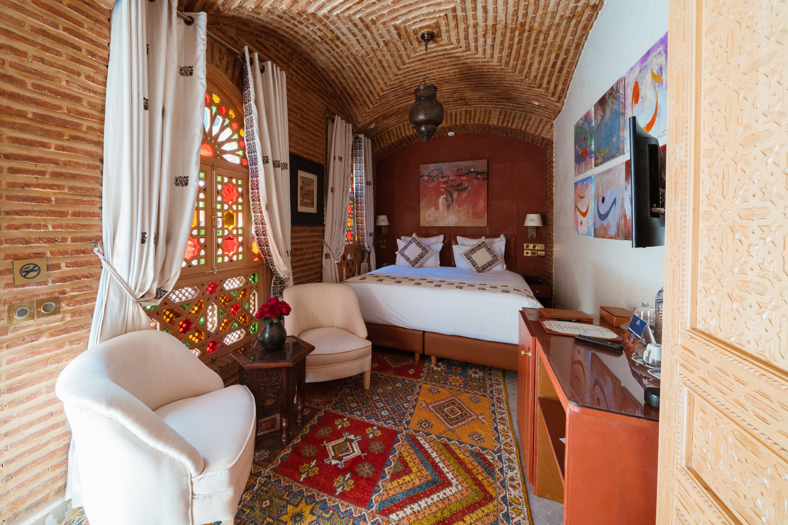 A traditional room with a bed, a chair, a desk, and a patterned carpet.