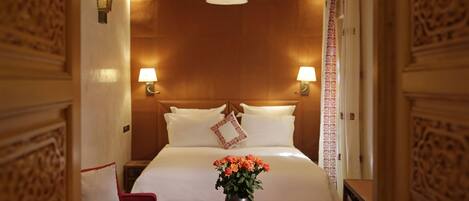 Una habitación de hotel con una cama grande, dos lámparas de noche, un florero con flores, un sofá rojo y un cabecero de madera.