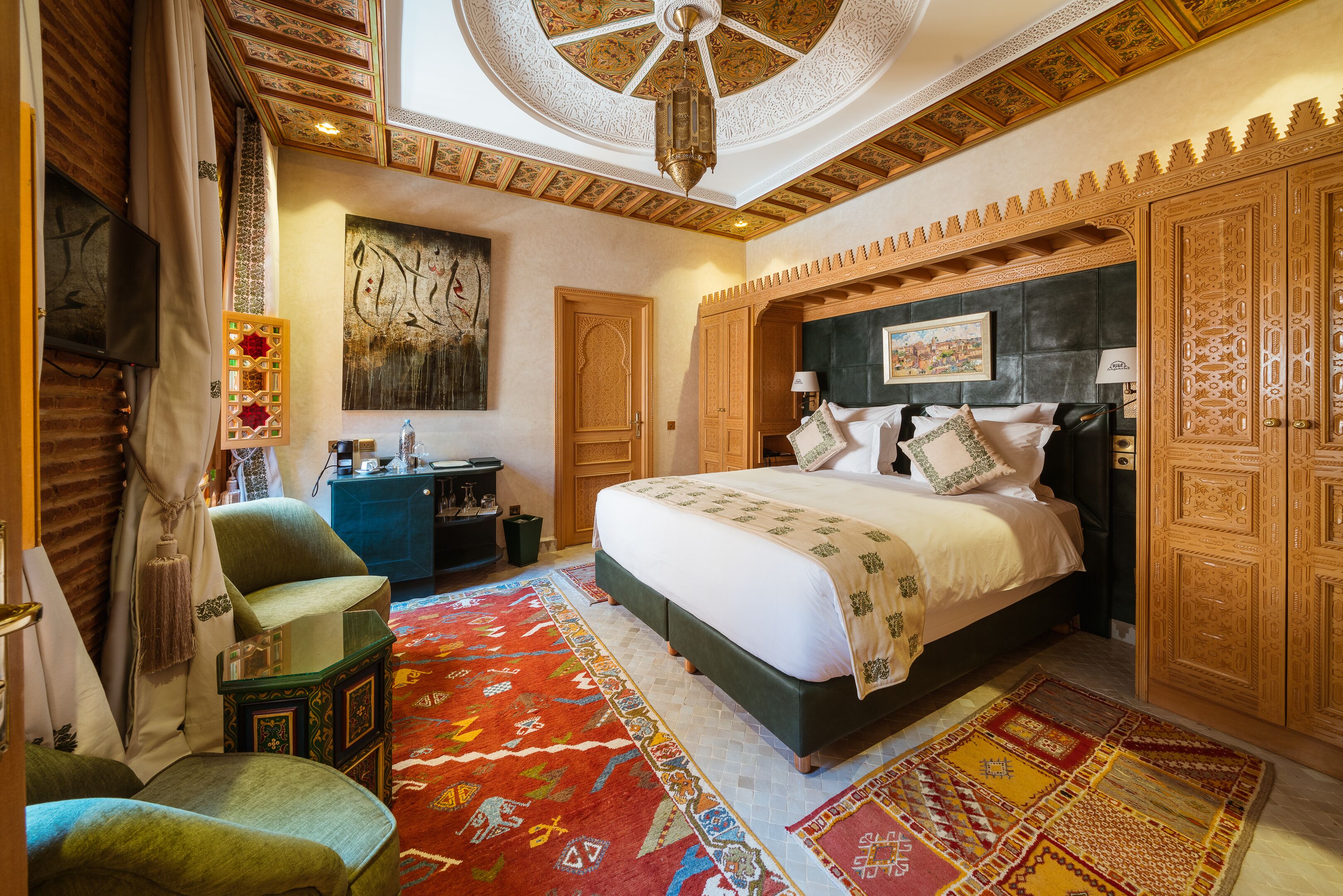 A spacious bedroom with a large bed, a television, a desk, and a decorative rug.
