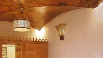 A room with a red sofa, a patterned rug, a wooden cabinet, and a ceiling with intricate designs.