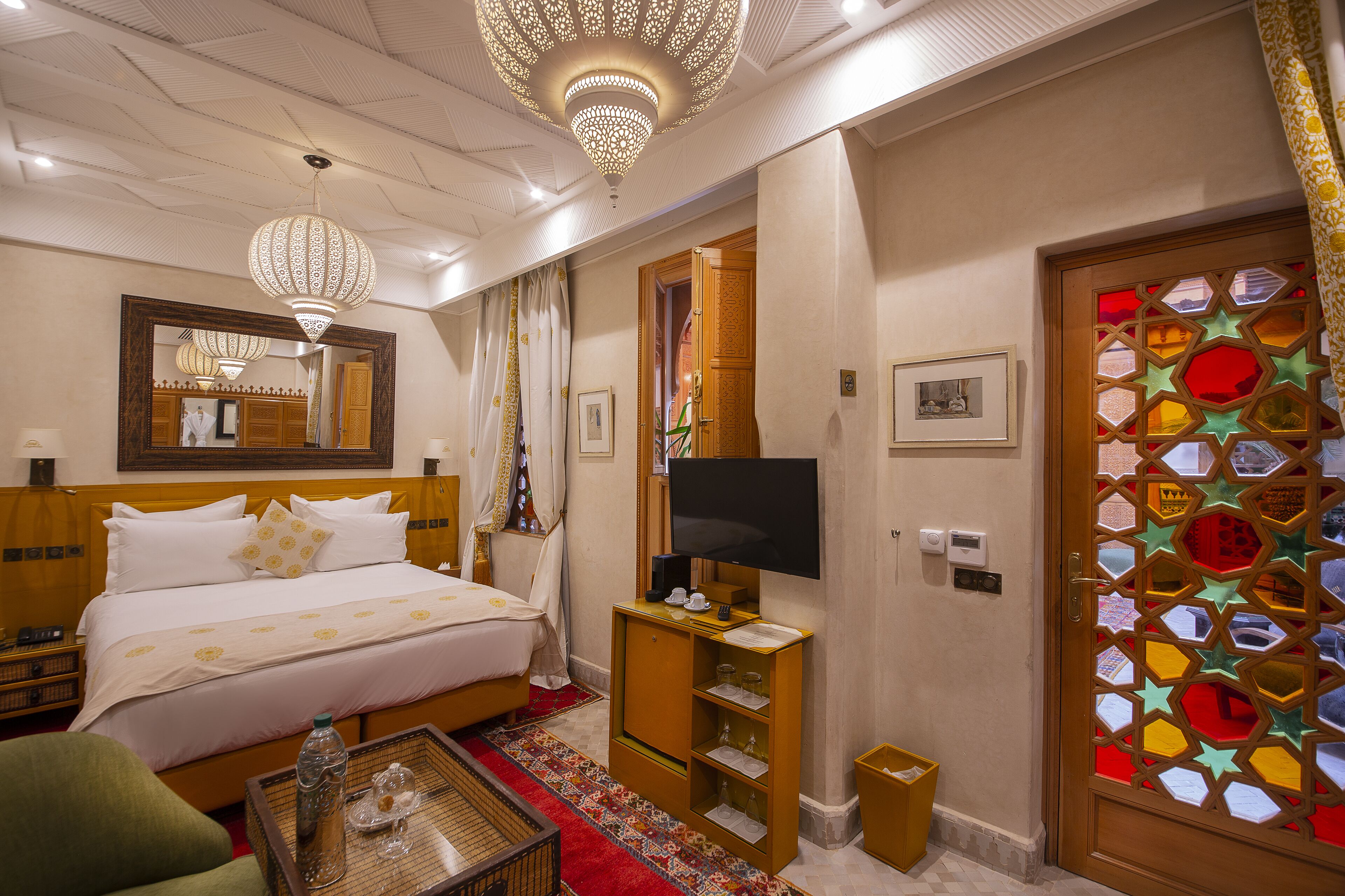 Une chambre d’hôtel comprenant un lit, une télévision, un miroir, une armoire en bois et une porte décorative.