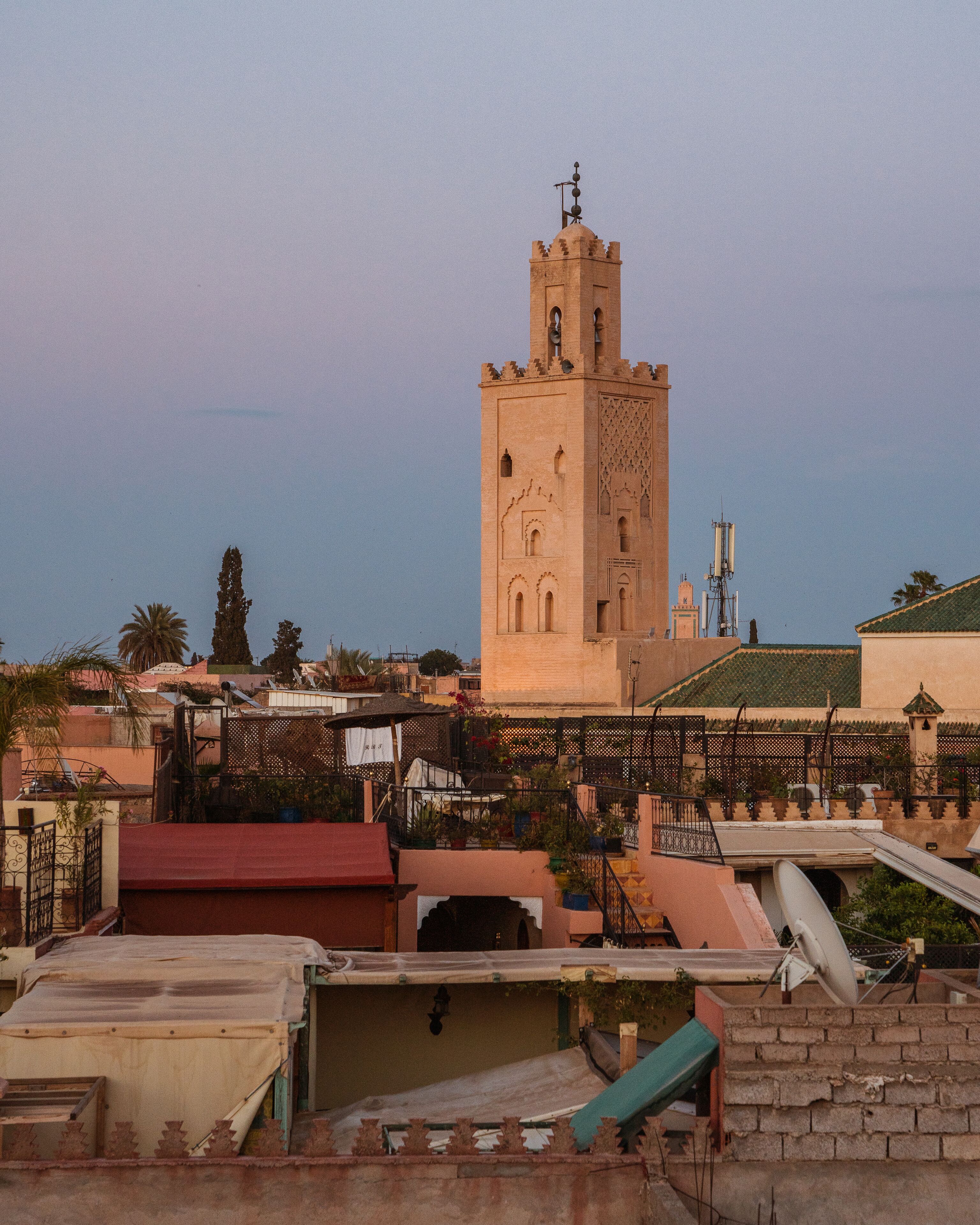A tower with a clock and a weather vane, surrounded by residential buildings with satellite dishes and a fence.