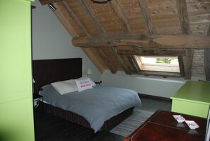 Relax in this cozy loft-style room featuring a plush bed, a bedside table, and a window with a view of lush greenery.