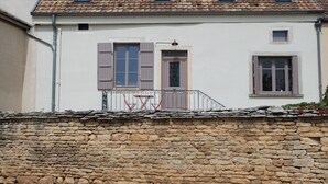 Un edificio de dos pisos con un muro de piedra en la fachada, techo de tejas y contraventanas en las ventanas.