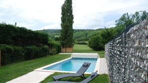 Una piscina con dos sillas de descanso y un muro de piedra.