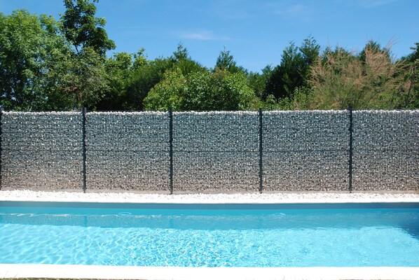 Relax by the pool surrounded by lush greenery and a natural stone wall.