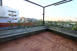 A rooftop terrace with a wooden floor, concrete steps, and a view of surrounding buildings and construction cranes. - Nilux Room - Hostel (Bangkok)