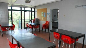 Ein Klassenzimmer mit Tischen und roten Stühlen, großen Fenstern und einem Bulletinboard.