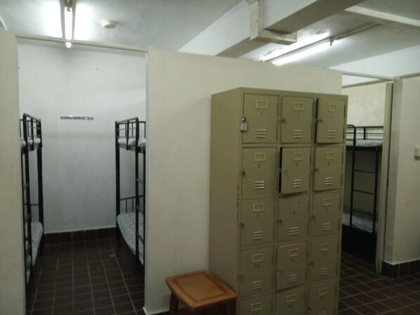 A dormitory room with bunk beds, a wooden stool, and a large stack of beige lockers.