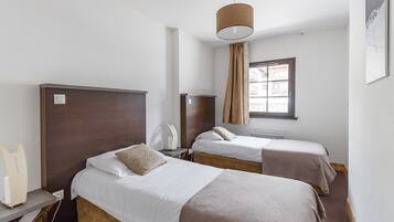 Ein Hotelzimmer mit zwei Betten, einem Schreibtisch mit Lampe, einem Fenster mit Vorhängen und einer Wandleuchte.