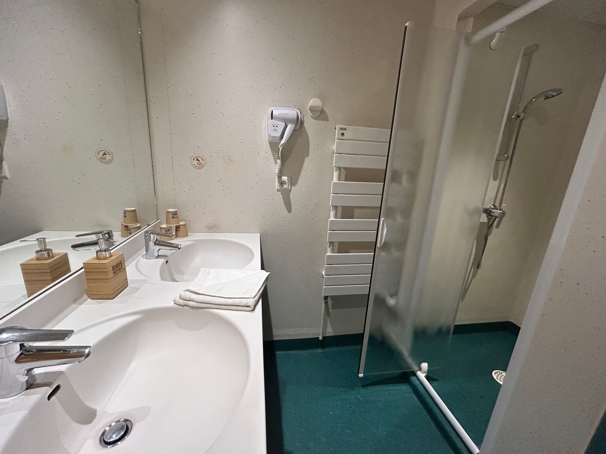 A bathroom with a white sink, mirror, and towel rack. There is a shower area with a glass door and a white towel hanging on the wall.