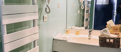 Un baño con un radiador blanco, un lavabo con espejo, un teléfono y un cubo de basura rojo.