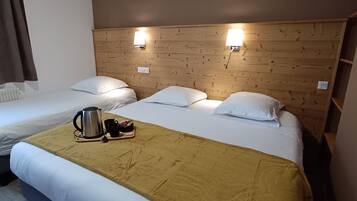 Habitación de hotel con dos camas individuales, cabecero de madera, lámparas de noche, cafetera y una manta marrón.