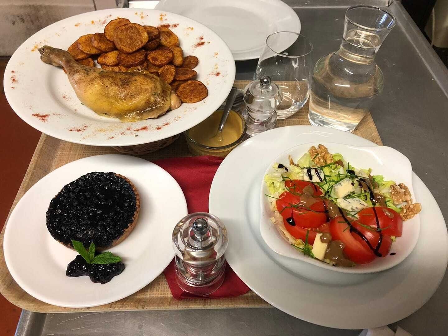 Una mesa con un plato de pollo asado, un plato de patatas asadas, un plato de morcilla y un plato de ensalada con tomates y nueces.