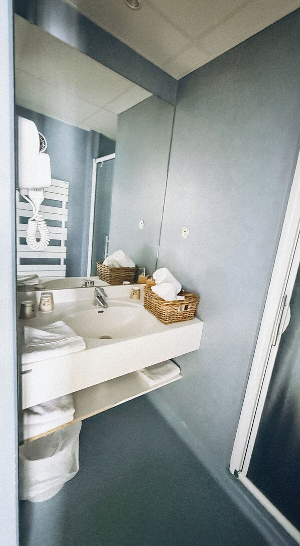 Un bany amb un lavabo blanc, un mirall i una cistella de productes de tocador.