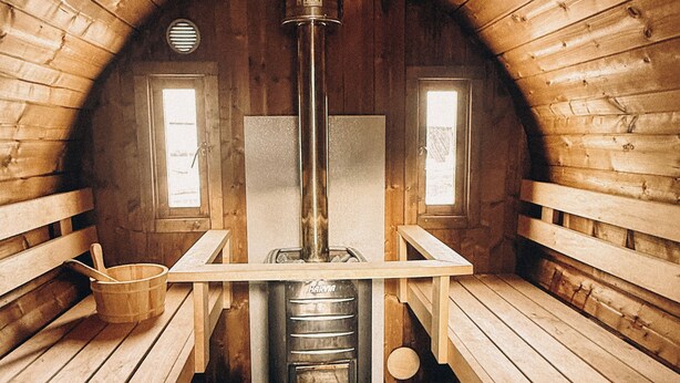 Una sauna con paredes y bancos de madera, un calentador central y dos ventanas.