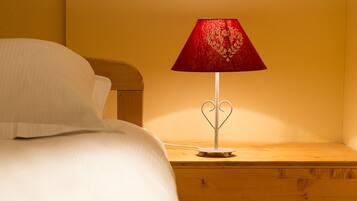 Un lit avec une literie blanche et une lampe en forme de cœur rouge posée sur une table de chevet en bois.