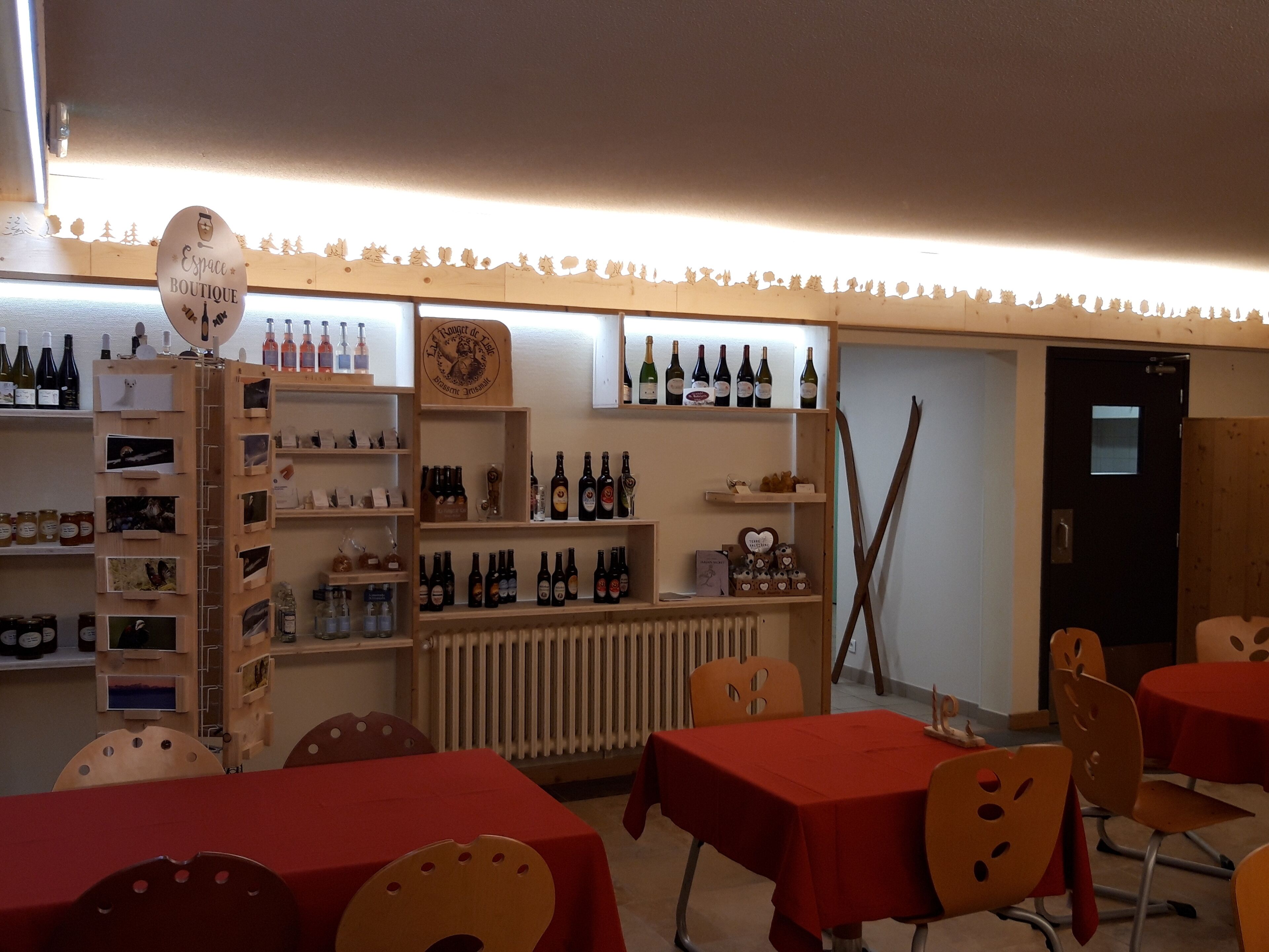 A restaurant with wooden shelves displaying bottles and food items, red tables, and chairs.