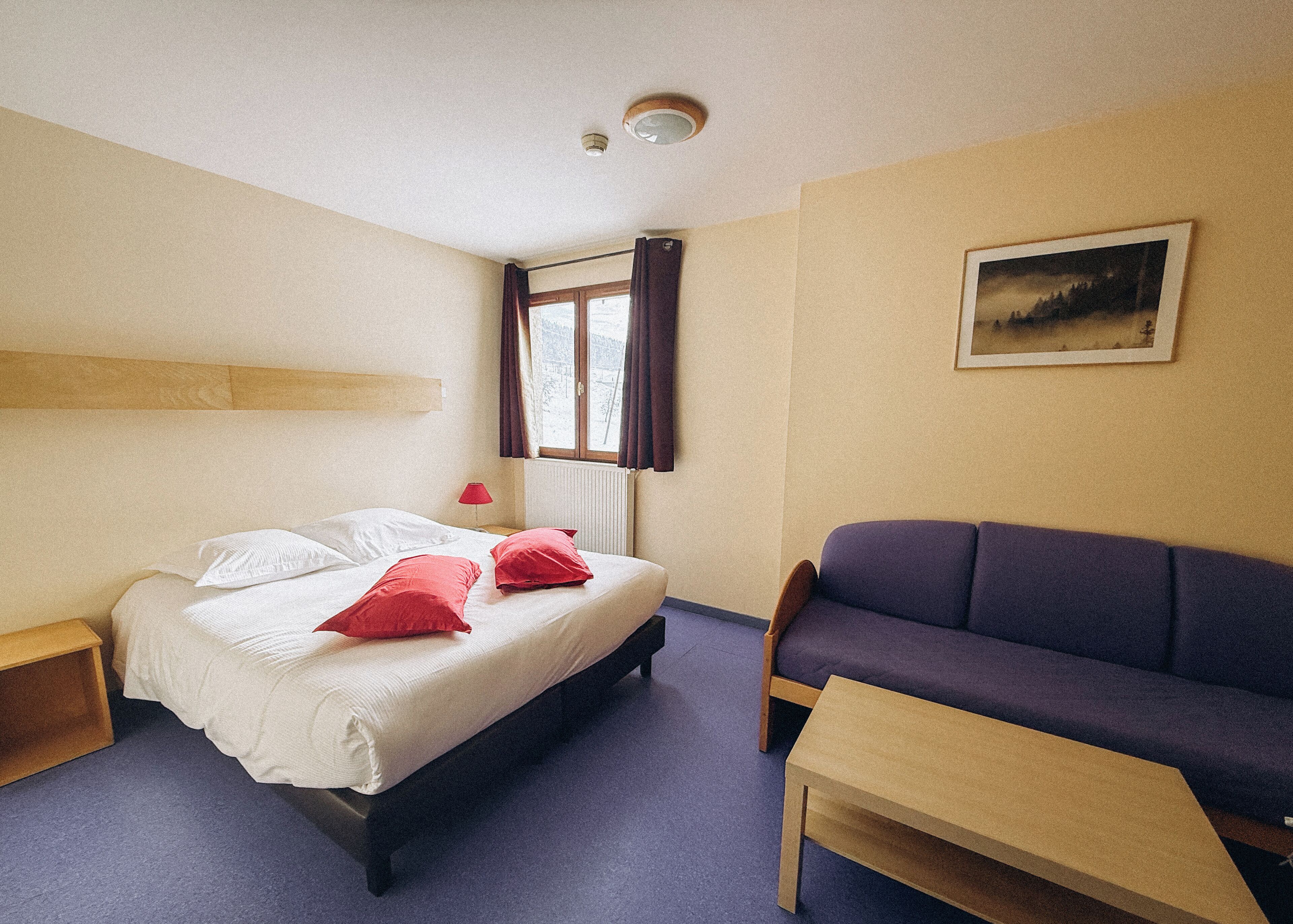 Une chambre d’hôtel avec un lit, un canapé, une table et une fenêtre avec des rideaux.